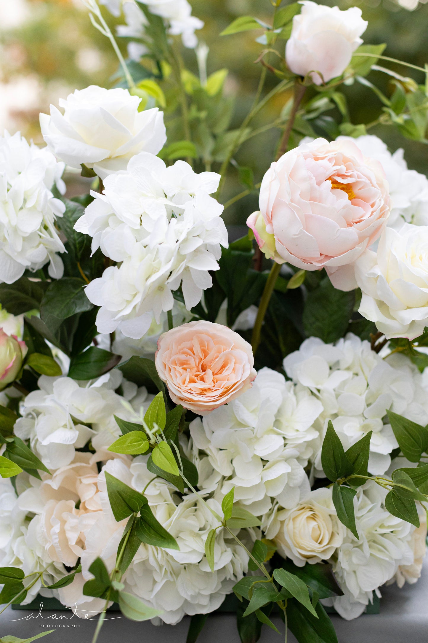 Wedding aisle flowers in a color palette of white, ivory, blush, and pale peach, accented by delicate vines.