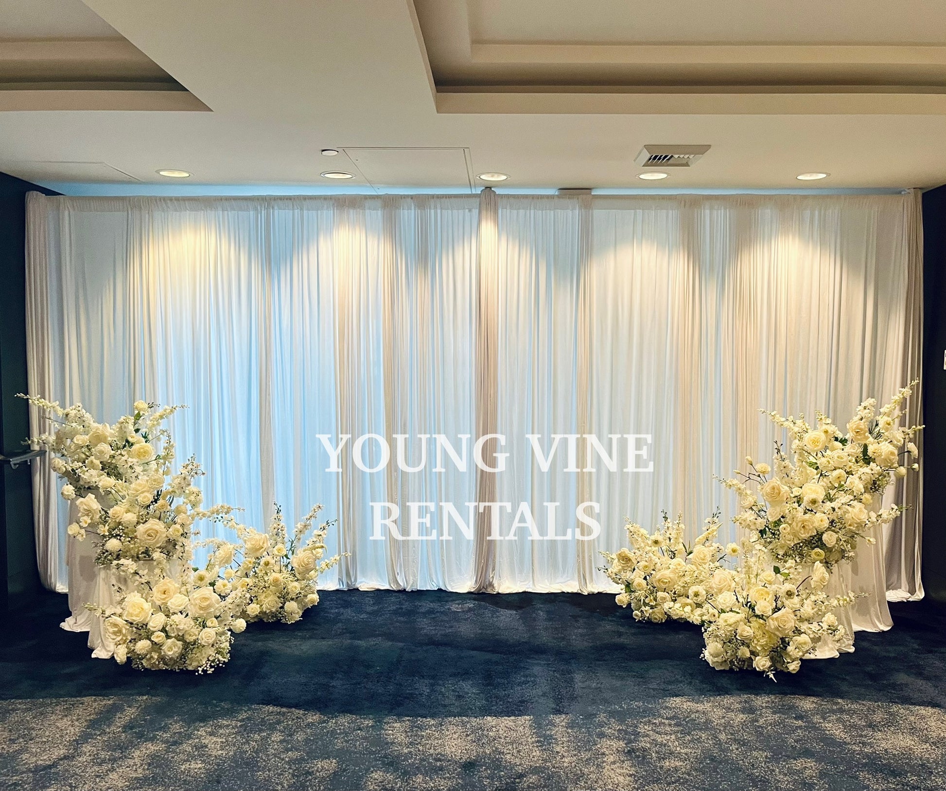 Decorative wedding floral arrangements in all white against a white draped backdrop