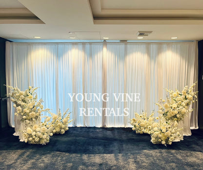 Decorative wedding floral arrangements in all white against a white draped backdrop