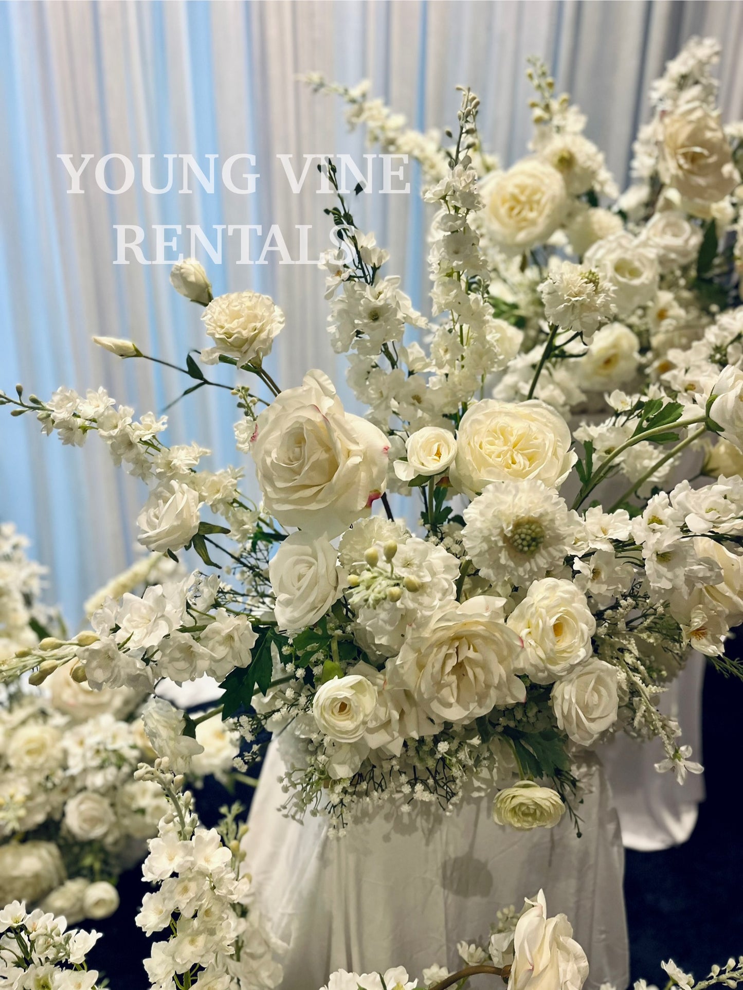 Decorative wedding floral arrangements in all white against a white draped backdrop