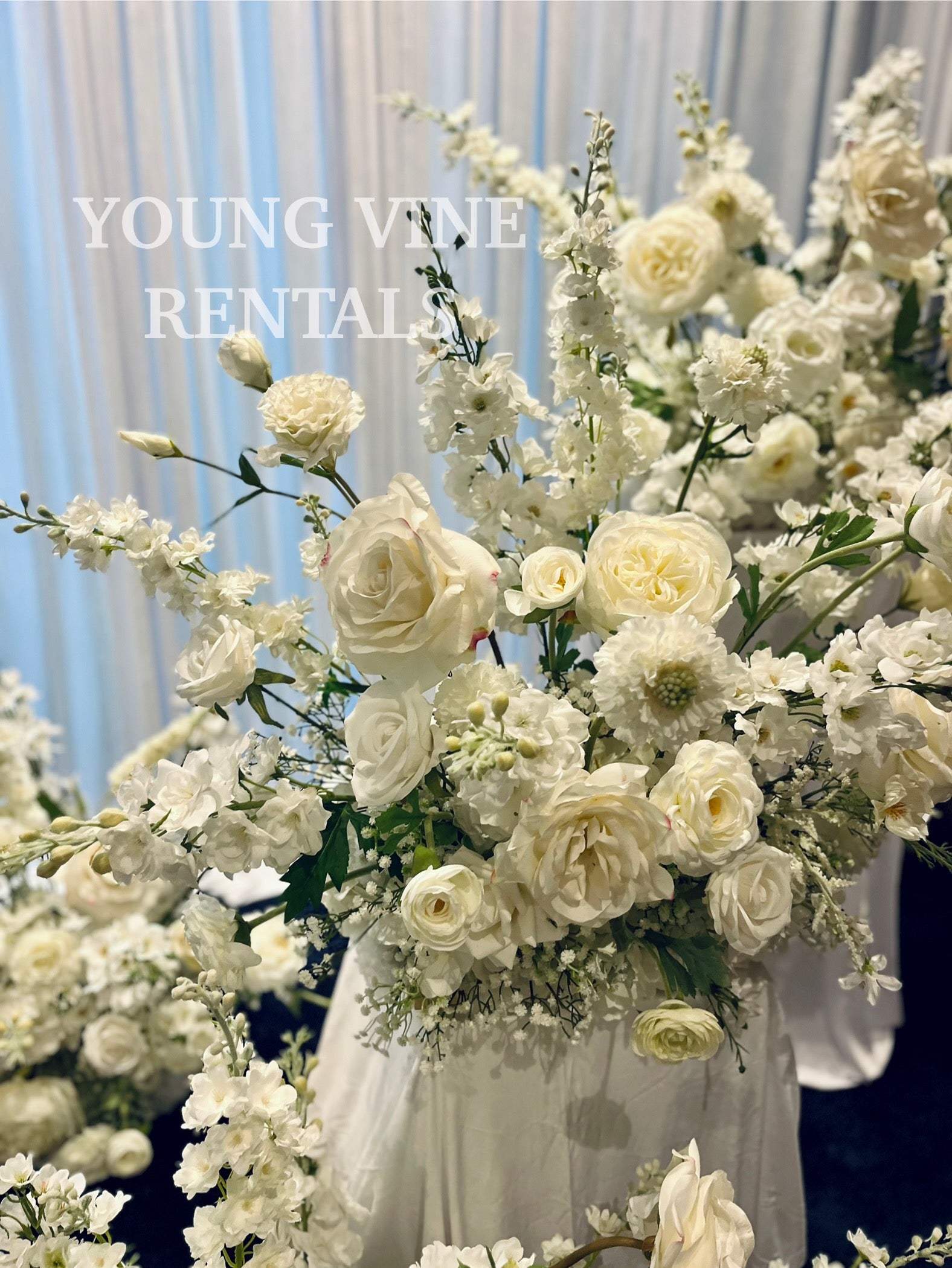 Decorative wedding floral arrangements in all white against a white draped backdrop